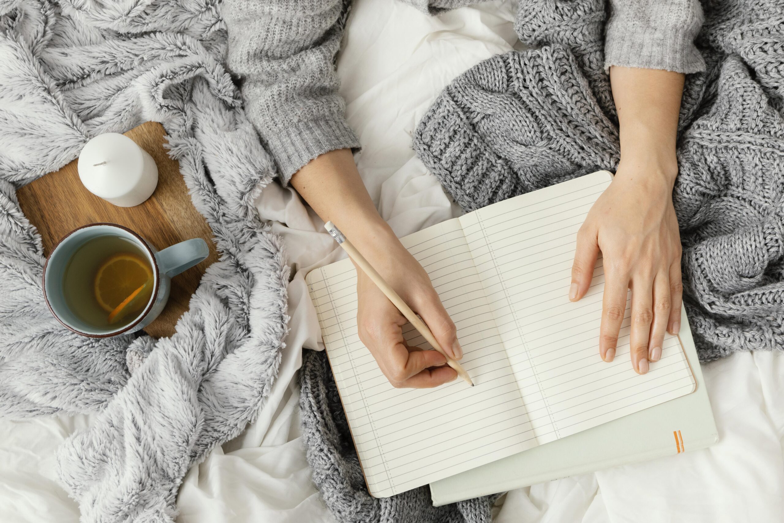 Beginners journal woman on a bed writing in a journal with a cup of tea and cozy blanket