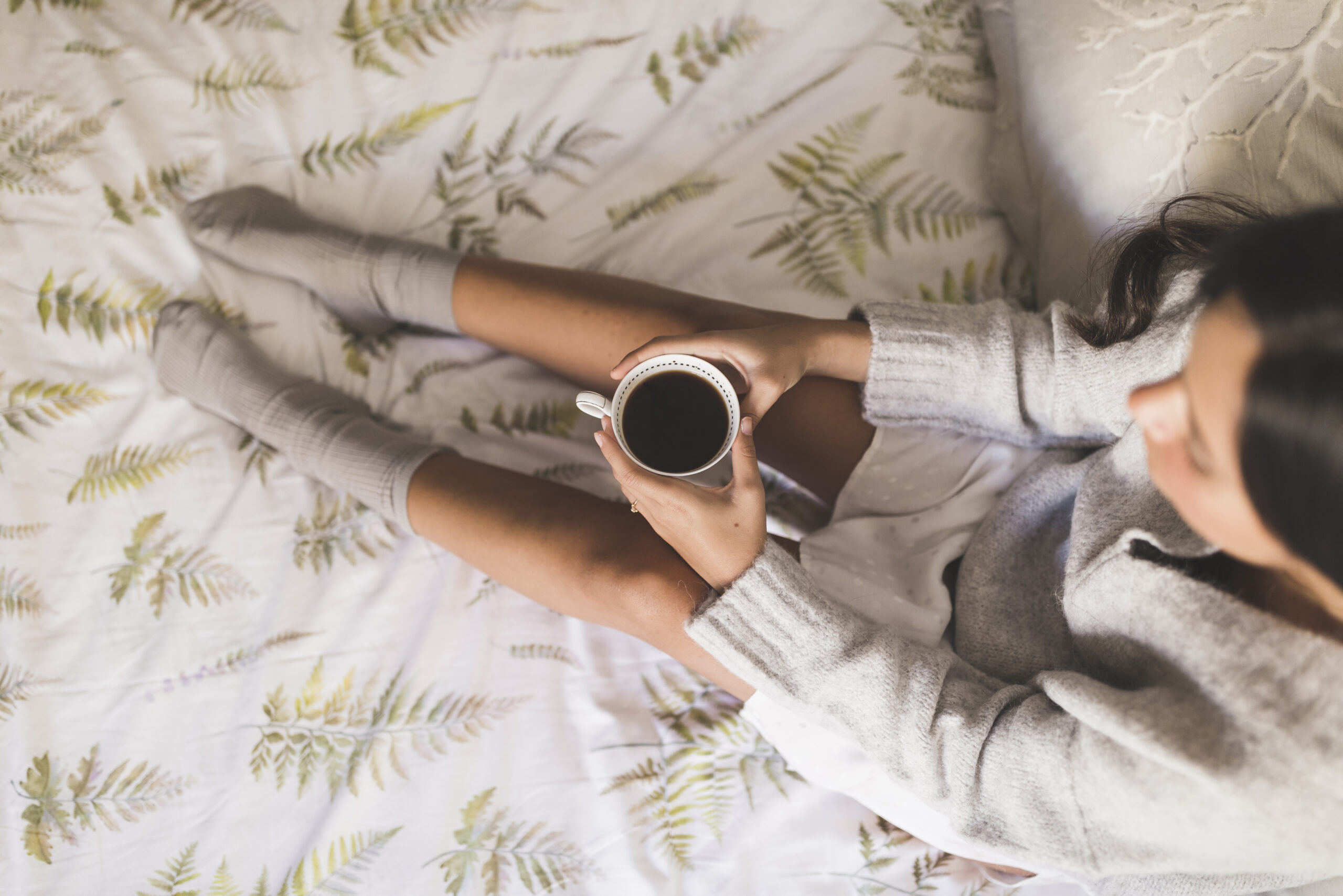 Stylish young woman in her 30s sitting cross-legged on a neatly made bed, wearing soft loungewear, looking relaxed but confident after getting better sleep habits